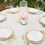 A table set with gold and white plates, silverware, and pink flowers.