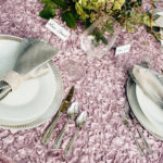 A table set with silverware and plates on top of pink fabric.