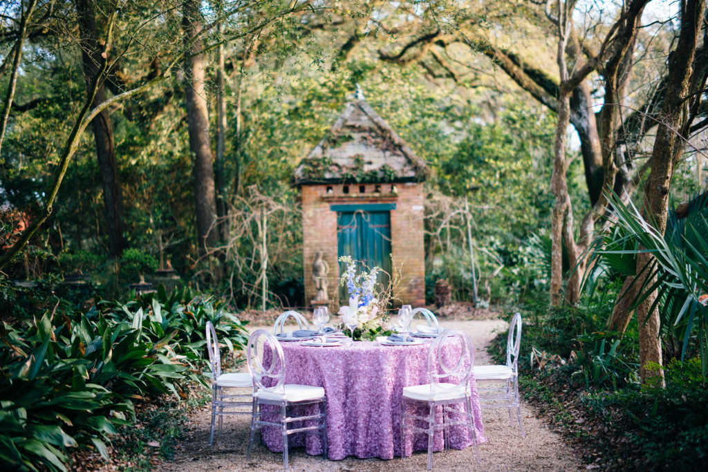 A table set up with purple linens and white chairs.