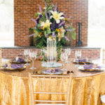 A table set with gold linens and a vase of flowers.